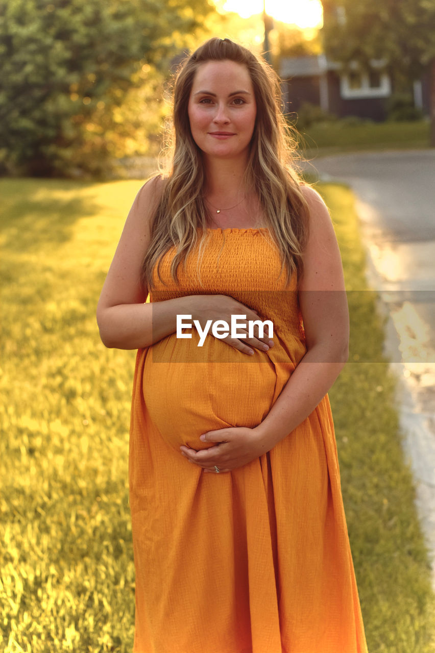 Portrait of pregnant woman with hands on stomach standing in park