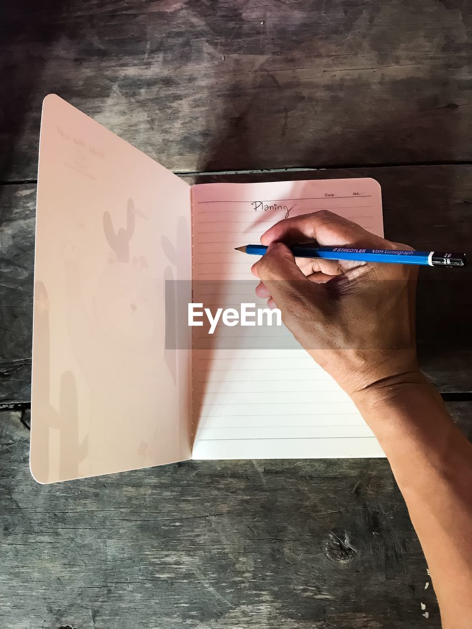 Cropped hand of man writing in diary on table