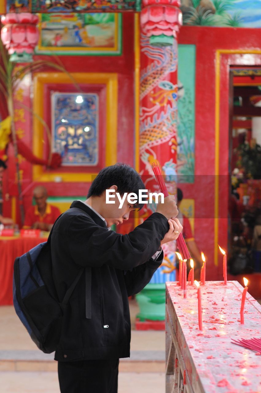 Side view of man igniting incense stick at temple