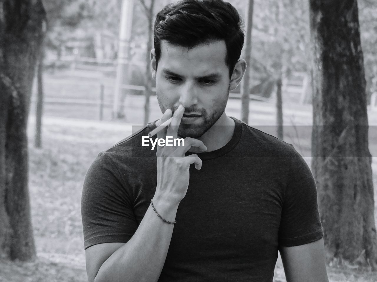 Close-up of young man smoking while standing amidst trees at park