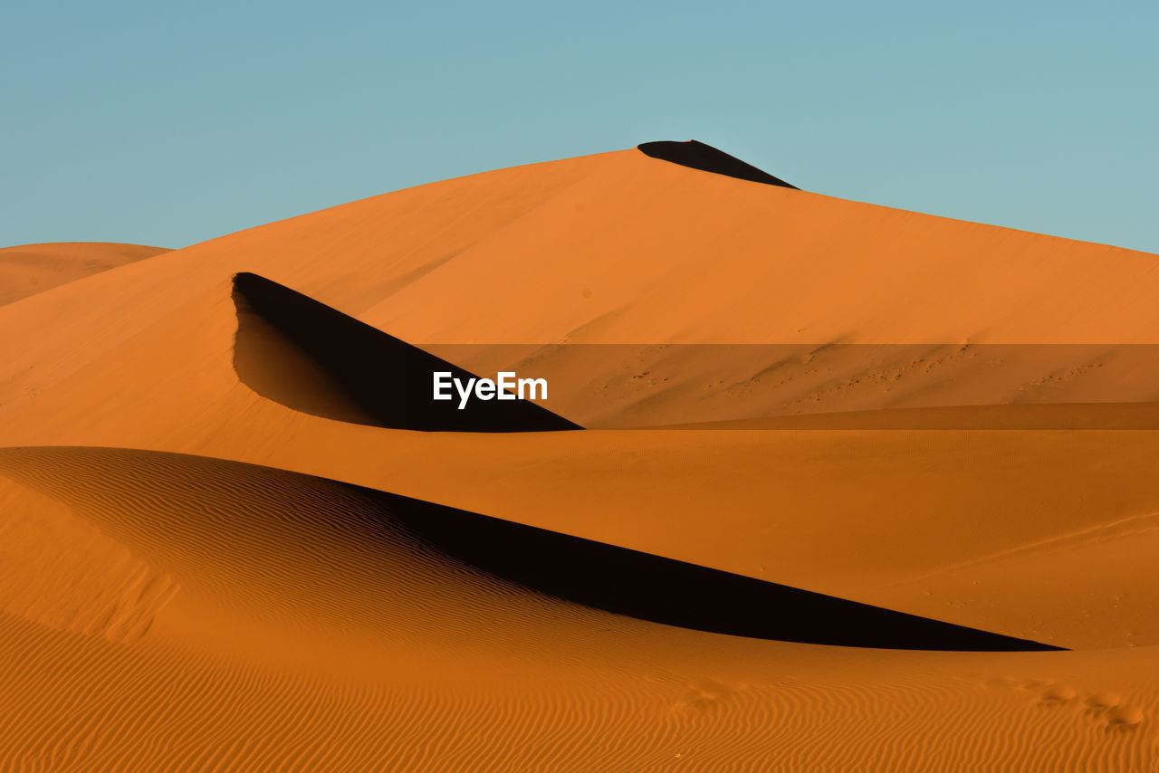 Low angle view of sand dunes against clear sky