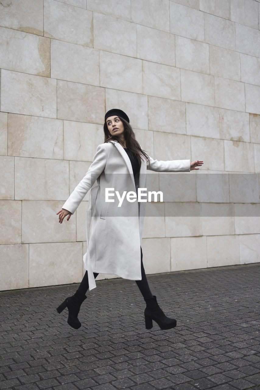 Young woman walking by wall on footpath