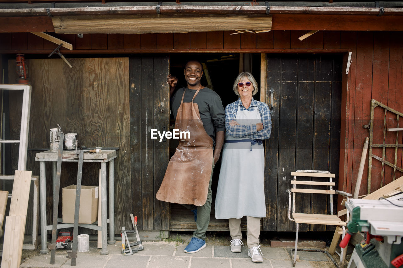 Full length portrait of smiling multi-ethnic coworkers standing at store entrance