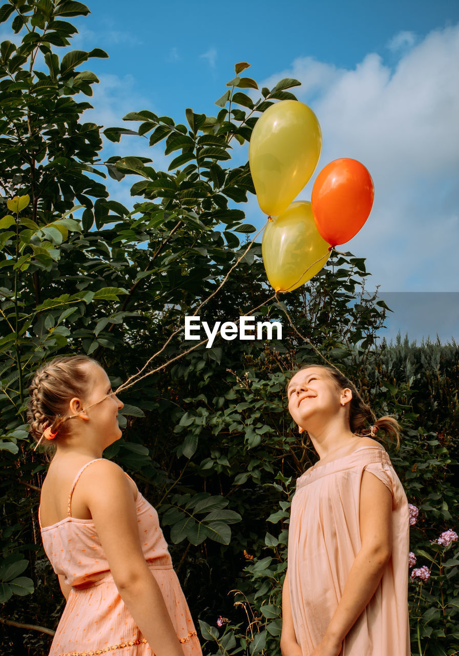 Two sisters in pink dresses and with balls tied to their braided hair are standing outside