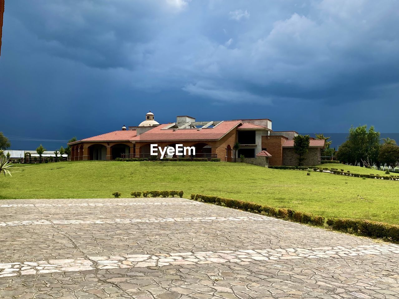 BUILDING ON FIELD AGAINST CLOUDY SKY