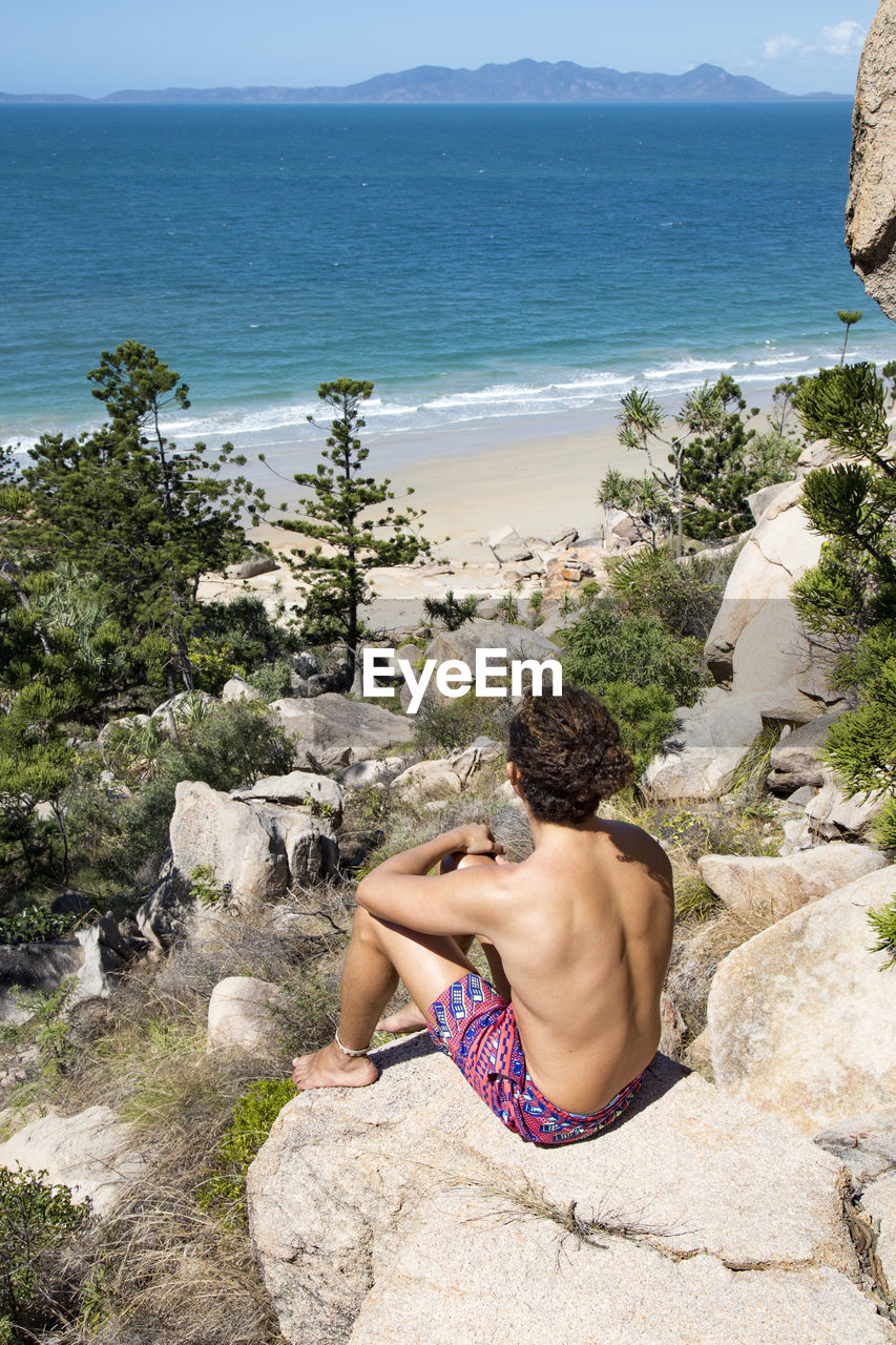 Young man with hair bun and bathing suit, looking at ocean view