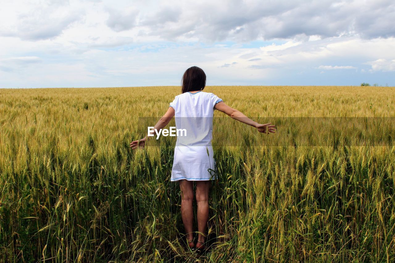 Rear view of woman standing in field against sky