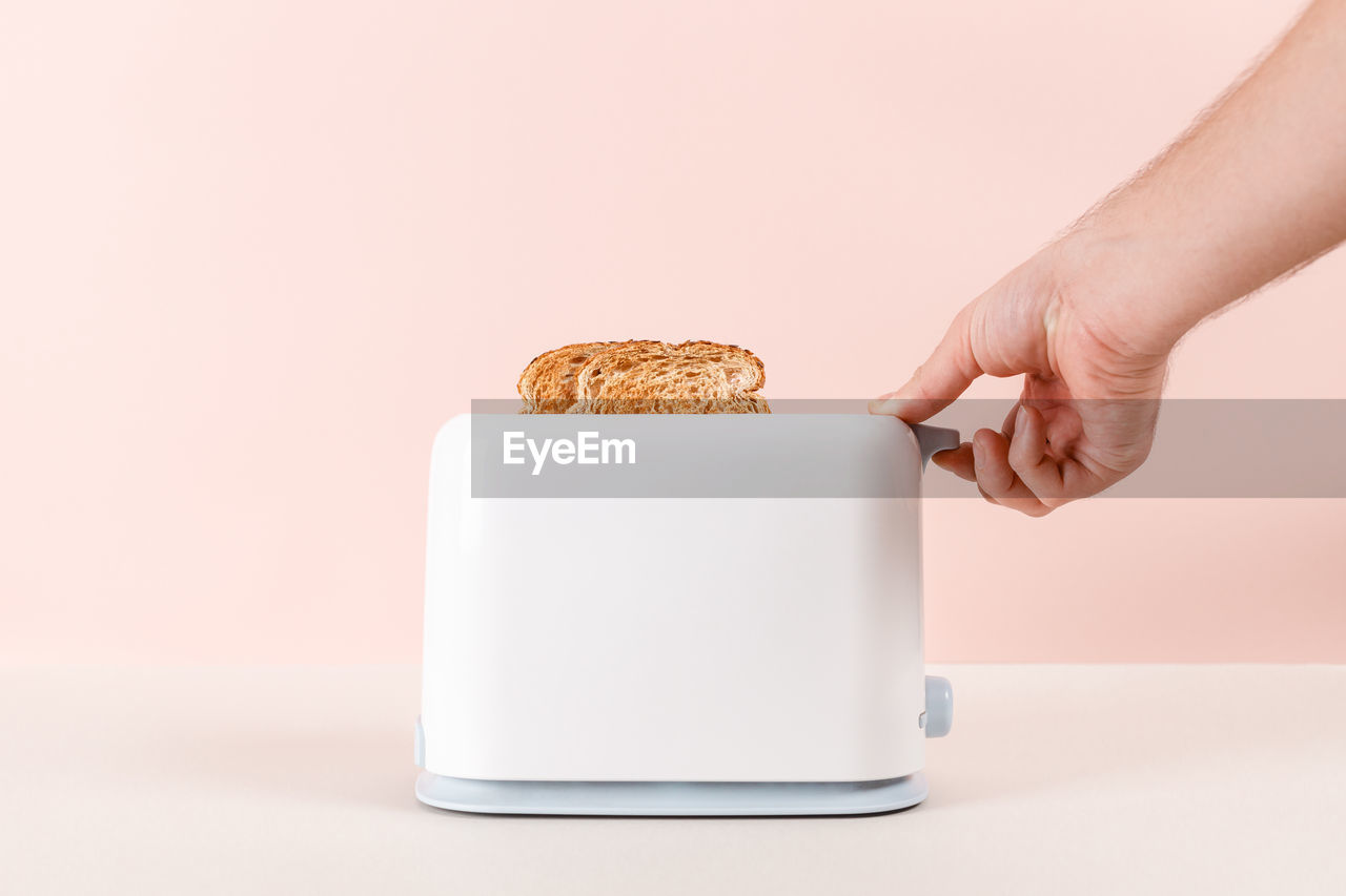 Man hand take out the bread out of the white toaster. delicious breakfast concept. pink background.