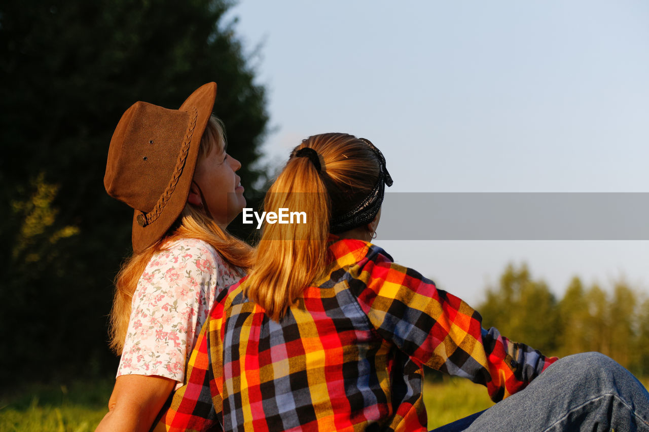 Back view of mother and daughter sitting on meadow and looking at green field. friendship love