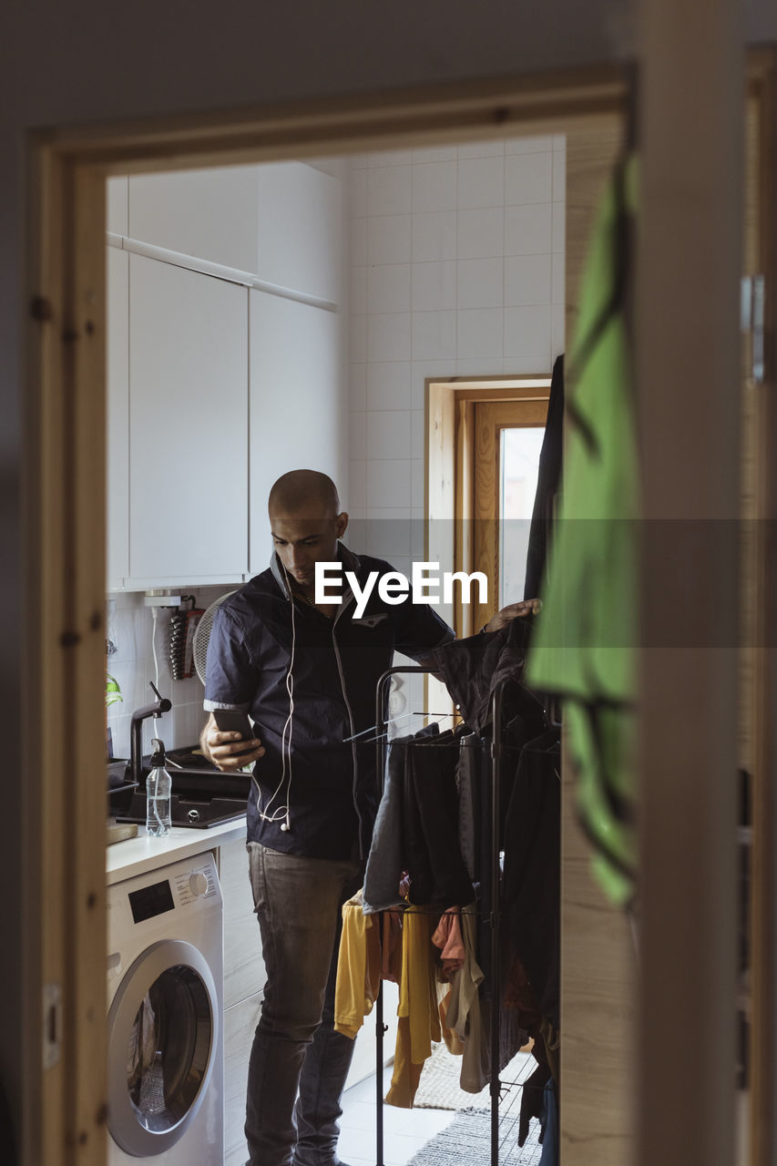 Man using smart phone while doing laundry chores in utility room