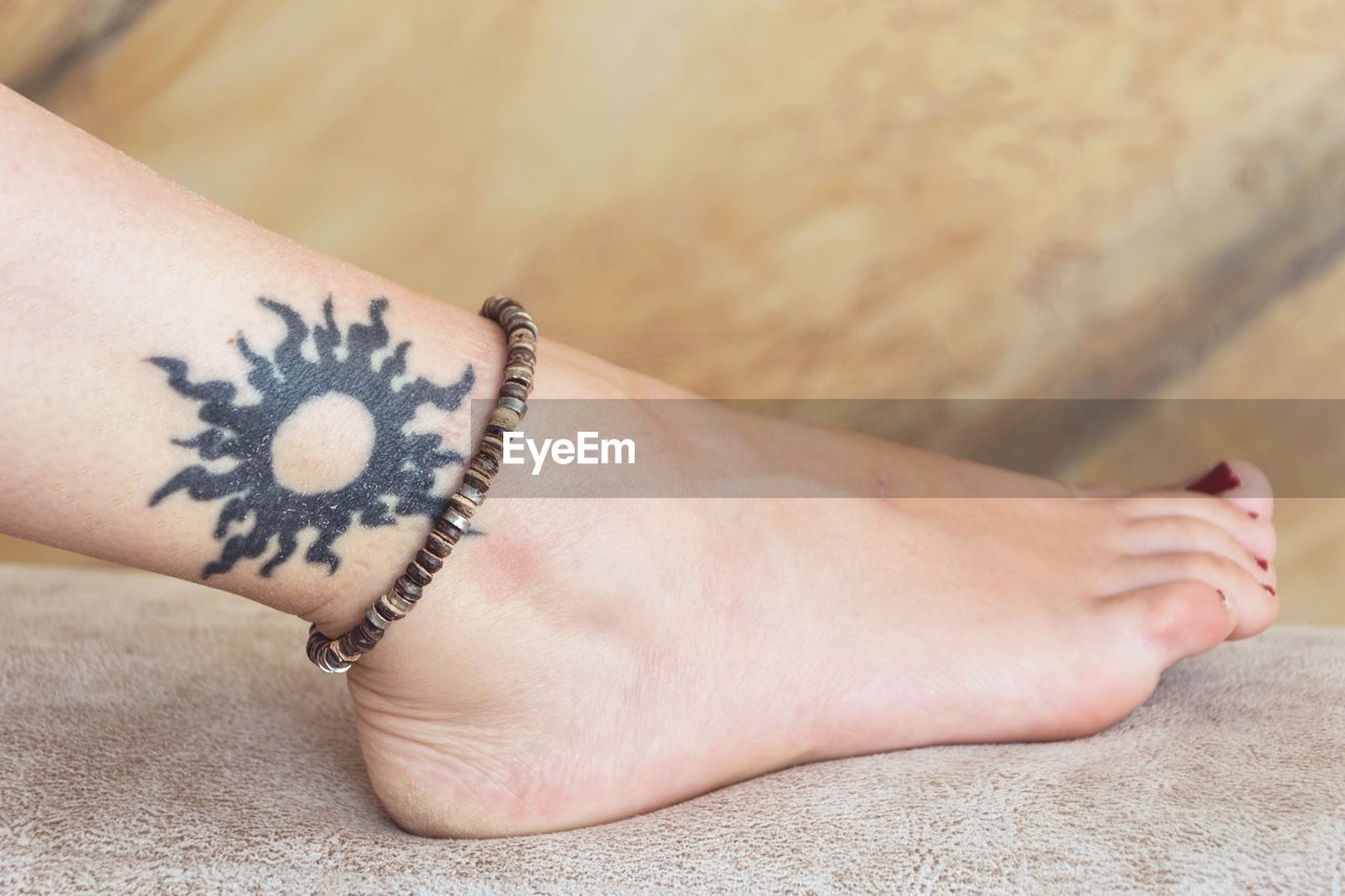 Low section of mid adult woman with tattoo wearing anklet