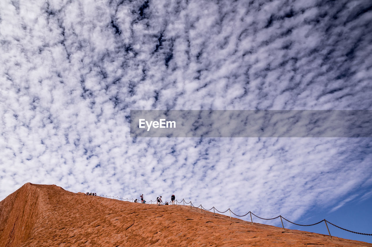 LOW ANGLE VIEW OF PEOPLE WALKING ON STREET AGAINST SKY