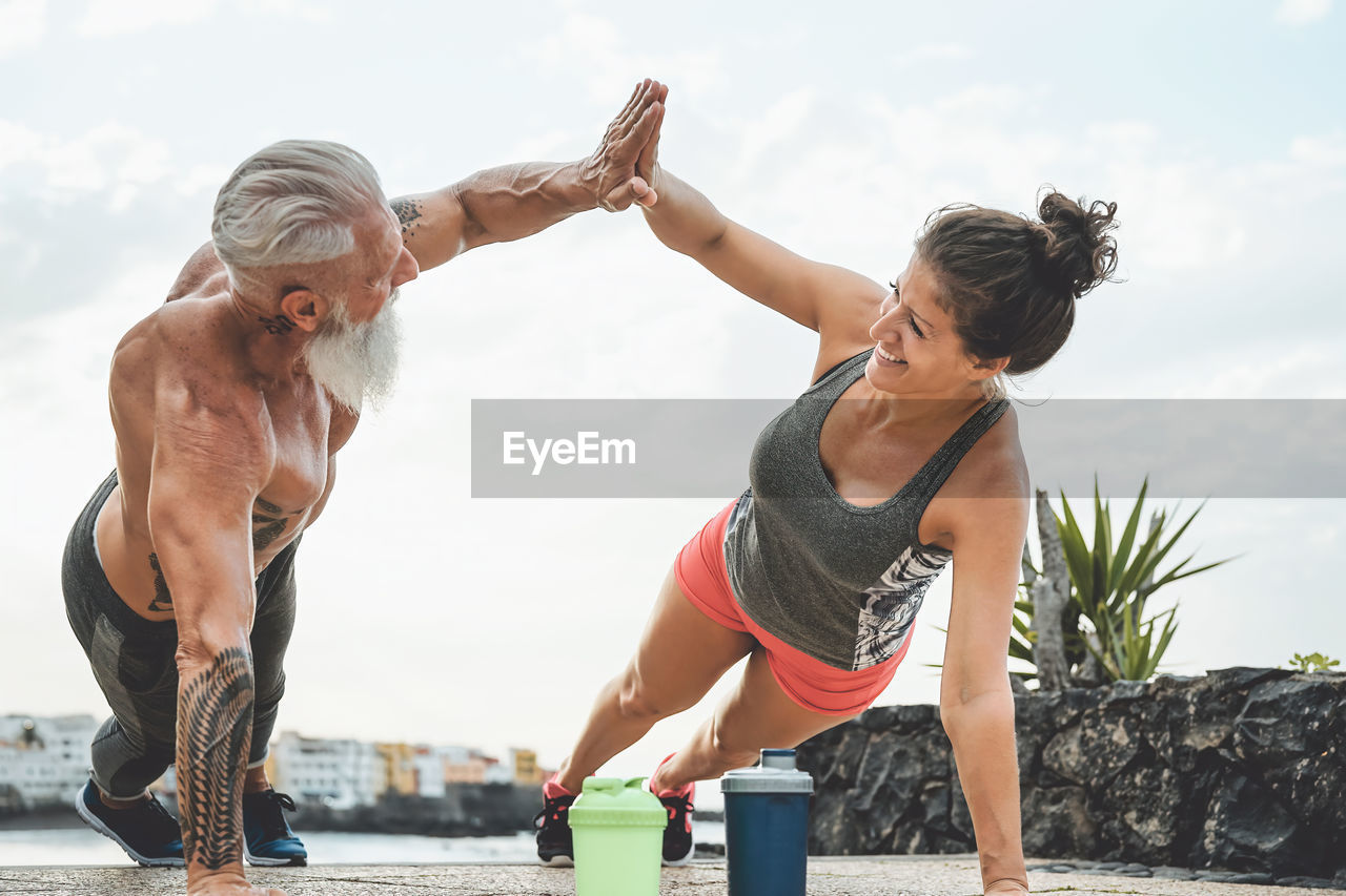 Man and woman giving high-five while exercising on land against sky