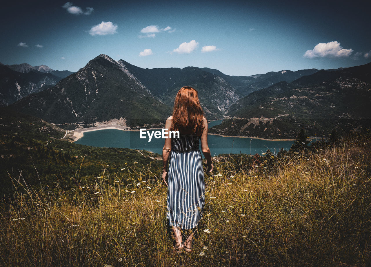 Woman standing on mountain against sky, staring at a lake