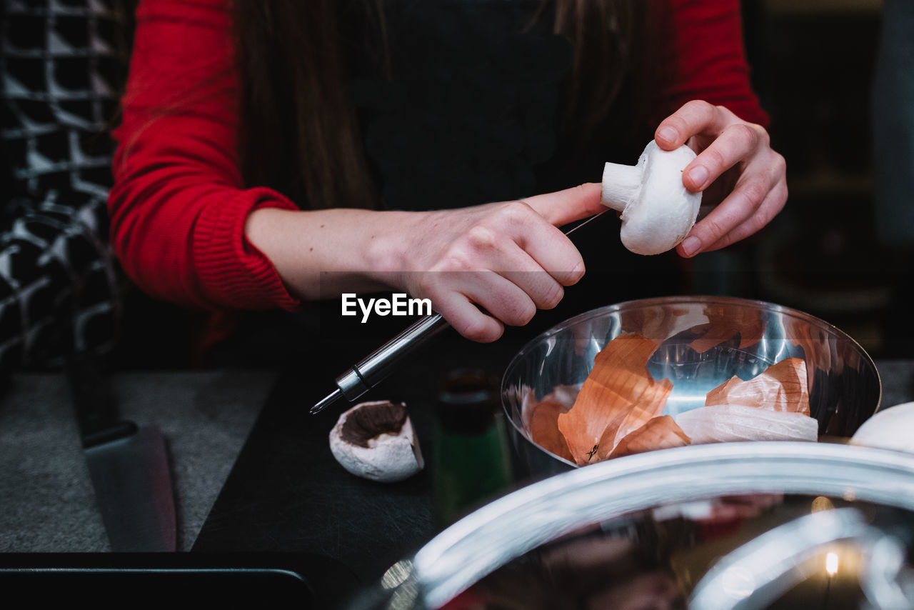 Unrecognizable female cleaning and mushroom over metal bowl during cooking course in restaurant kitchen in navarre, spain