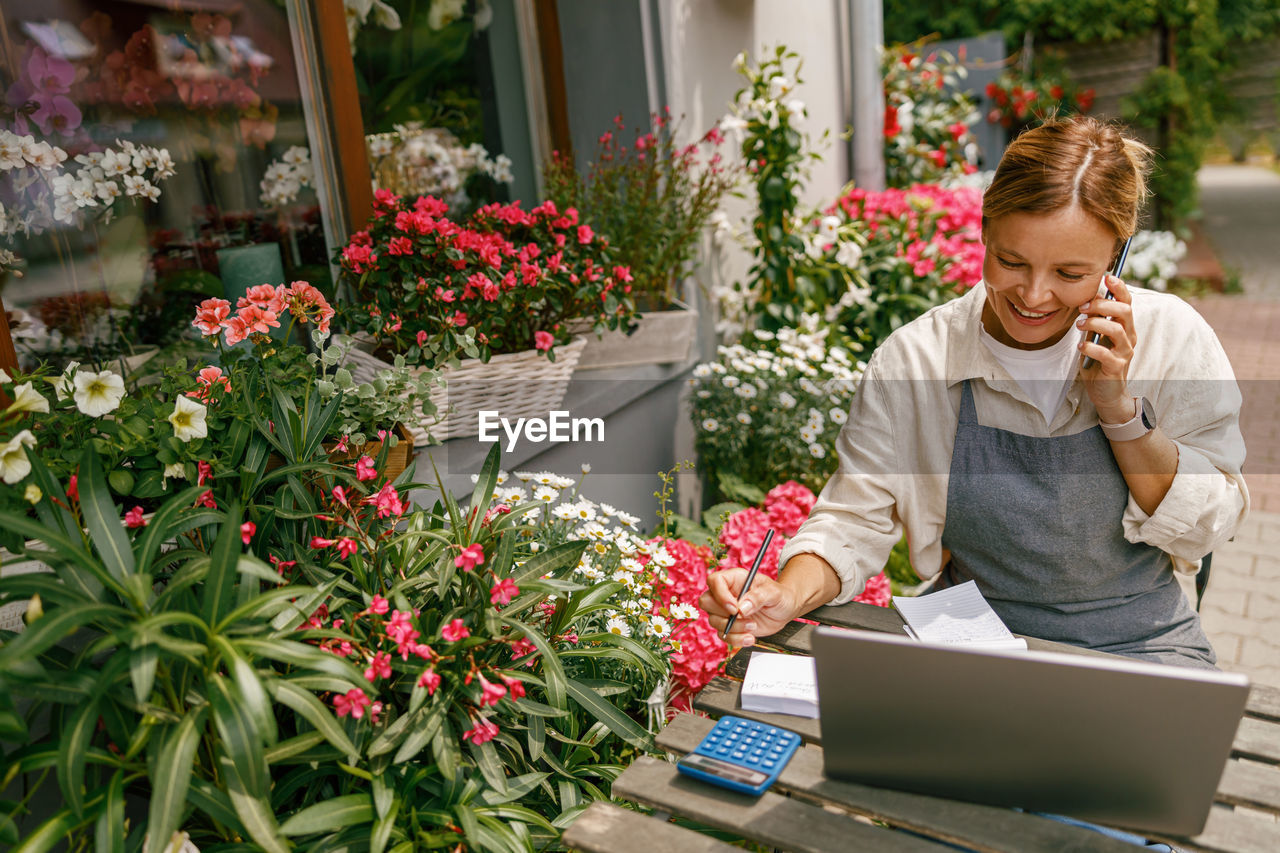 young woman using mobile phone while standing by plants