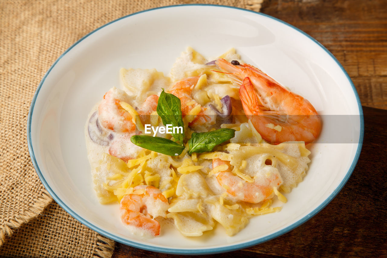 Farfalle pasta with shrimps in a creamy sauce on a gray plate on a wooden table on a linen napkin