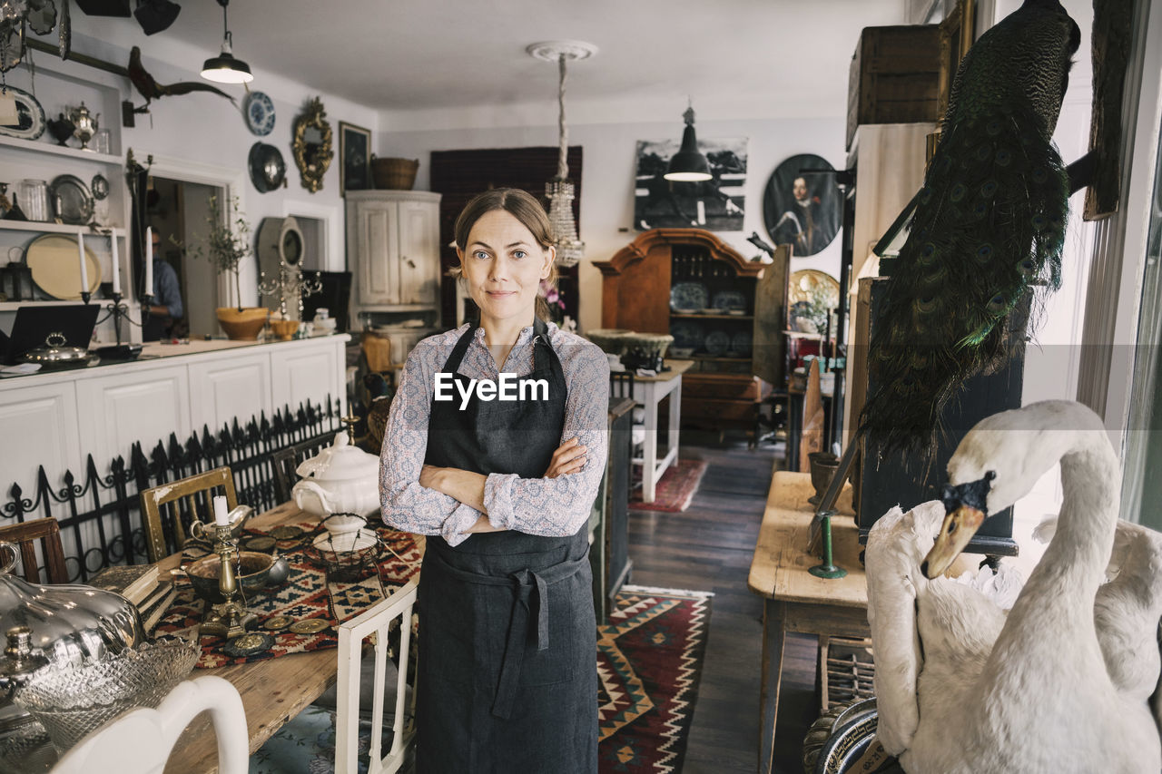 Portrait of female retailer with arms crossed standing in antique shop