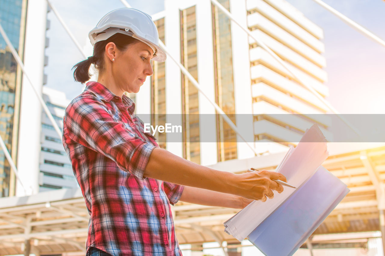 Female engineer holding blueprint while standing in city