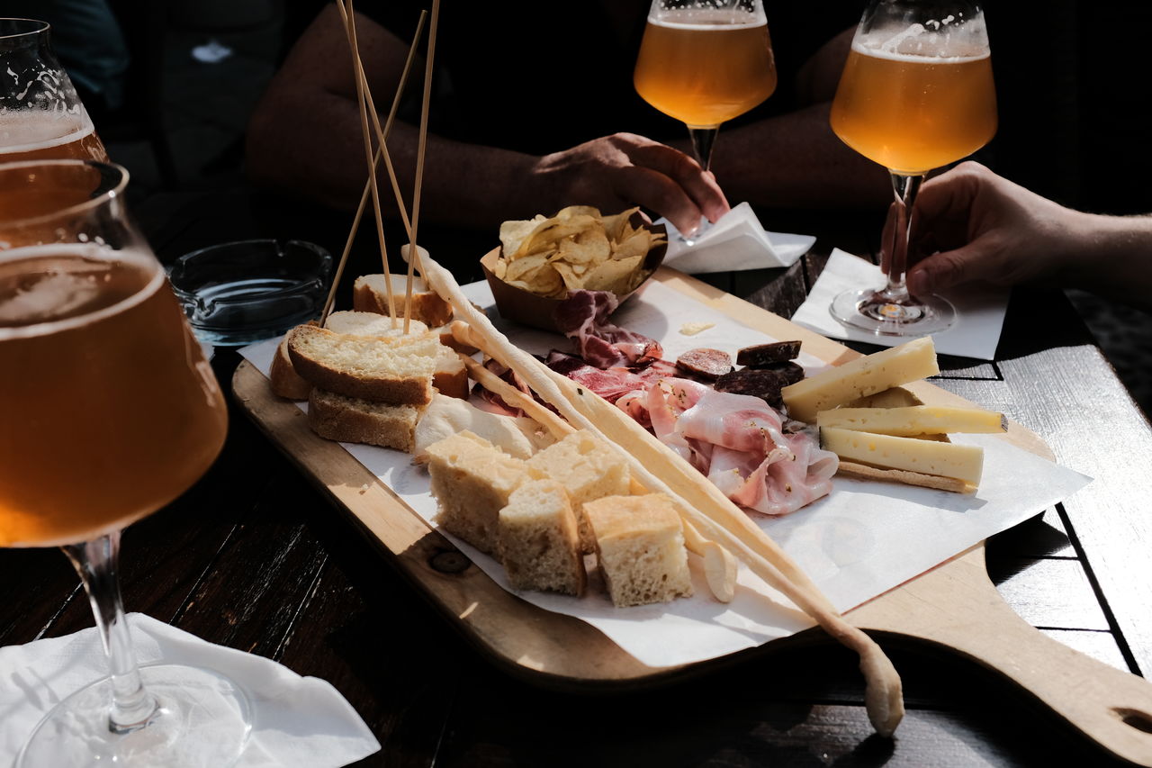 Cropped hands of friends holding beer glass by food on table at bar