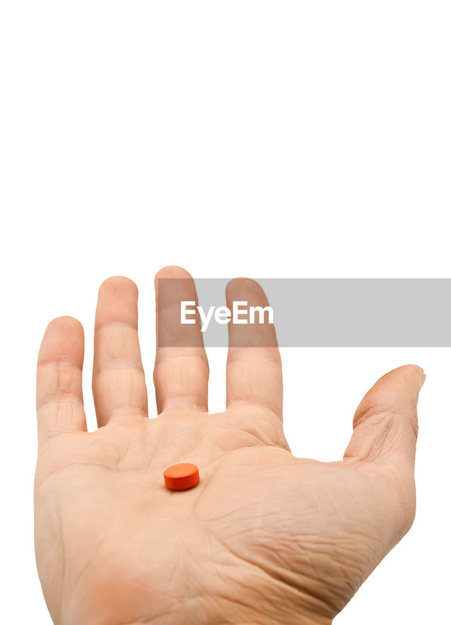 Close-up of hand holding pill against white background