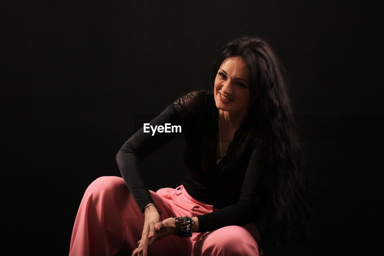adult, one person, women, sitting, black background, performing arts, studio shot, indoors, long hair, photo shoot, performance art, copy space, stage, hairstyle, entertainment, female, young adult, emotion, portrait, person, darkness, looking, singing, lifestyles, three quarter length, brown hair, fashion, black, clothing, sadness, modern dance