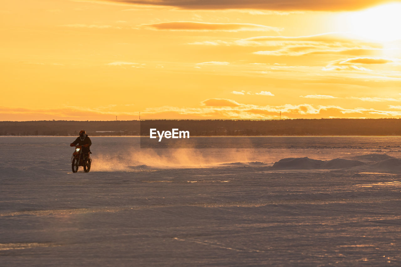 Motocrosso on frozen lake against sky during sunset