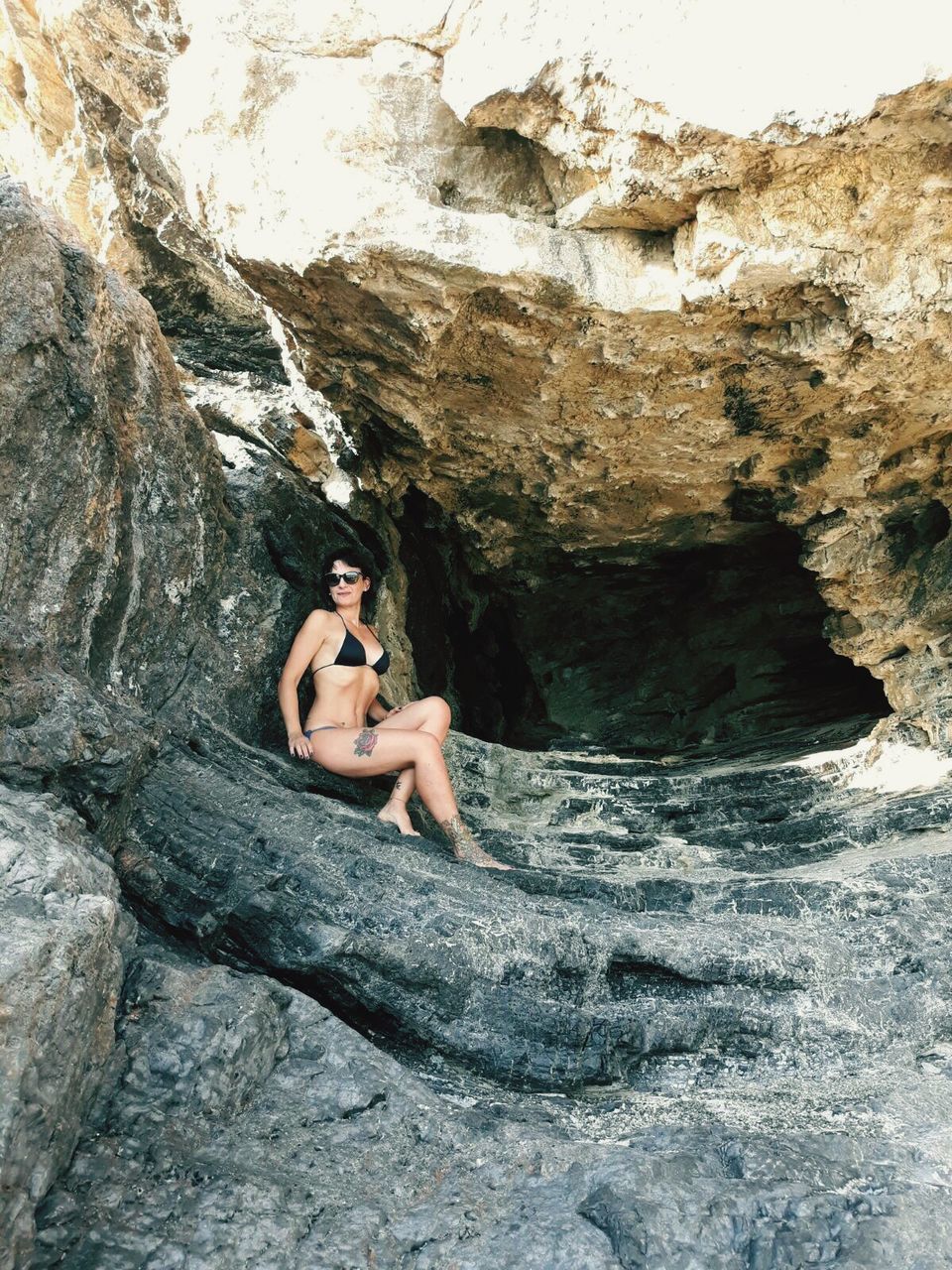 Young woman in bikini sitting on rock formation at spiaggia del troncone