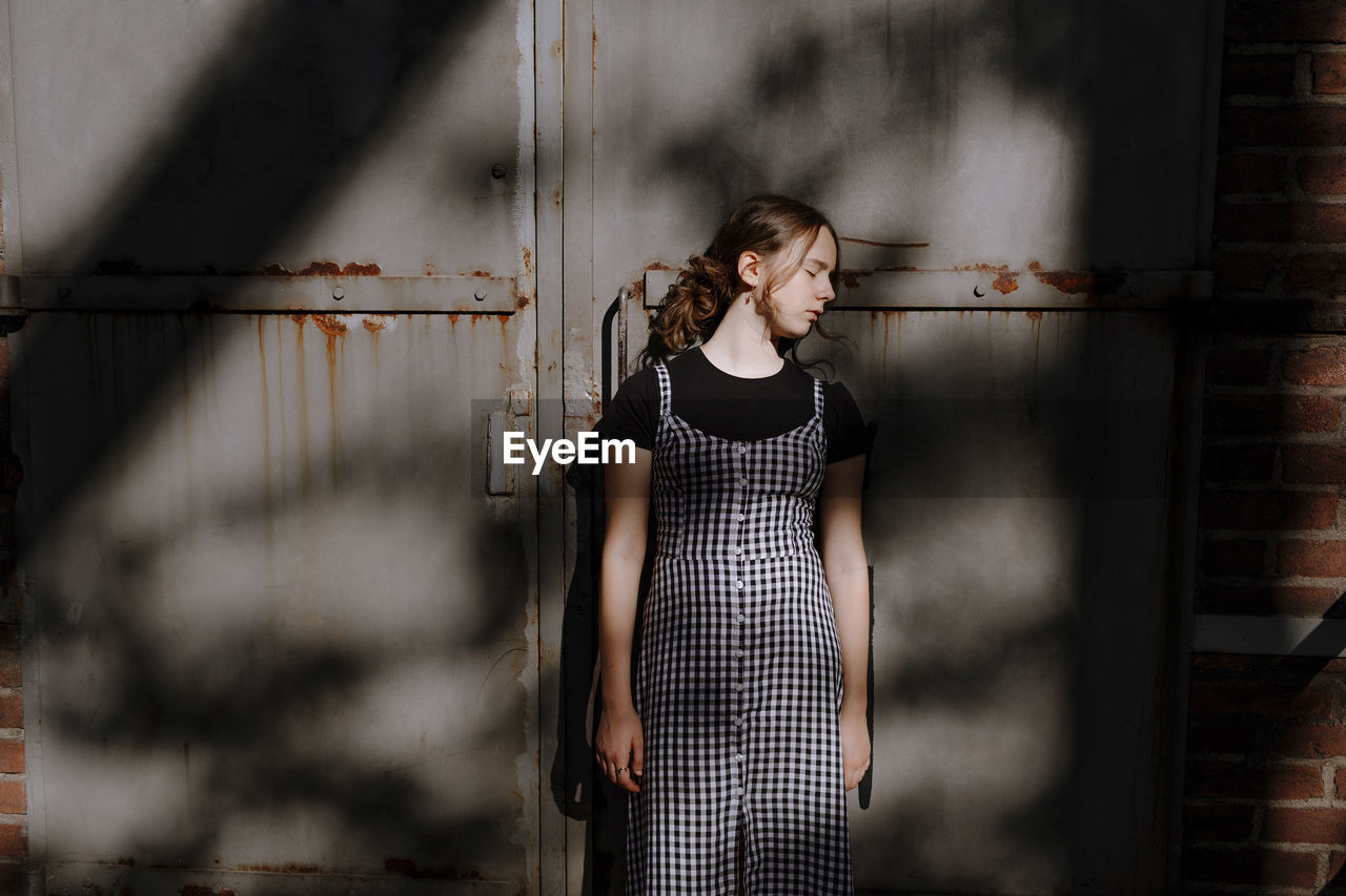 Teenage girl with eyes closed standing against rusty metallic wall