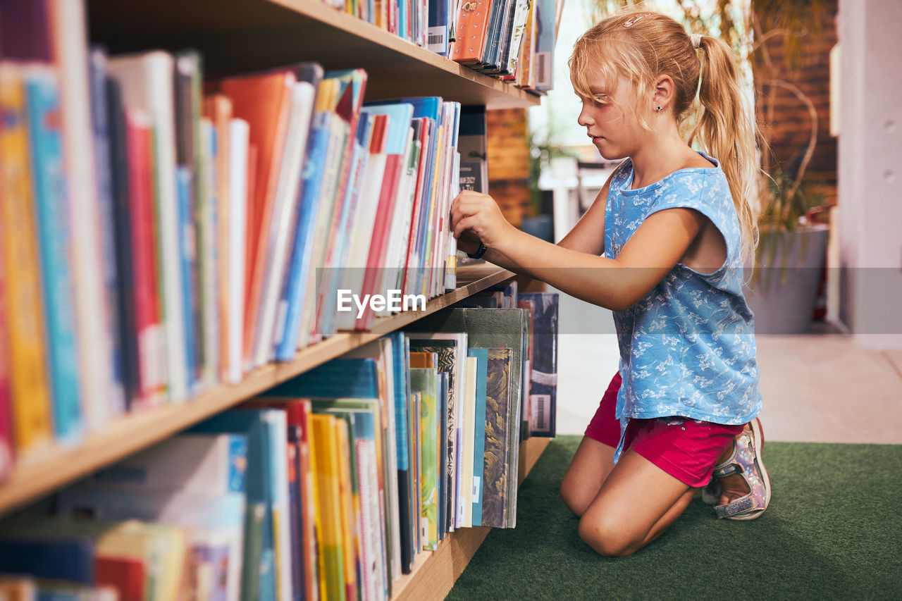 Schoolgirl looking for book for reading in school library. student selecting literature for reading