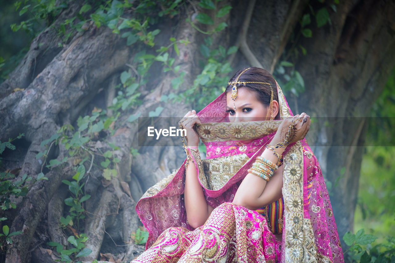 Portrait of bride sitting against tree