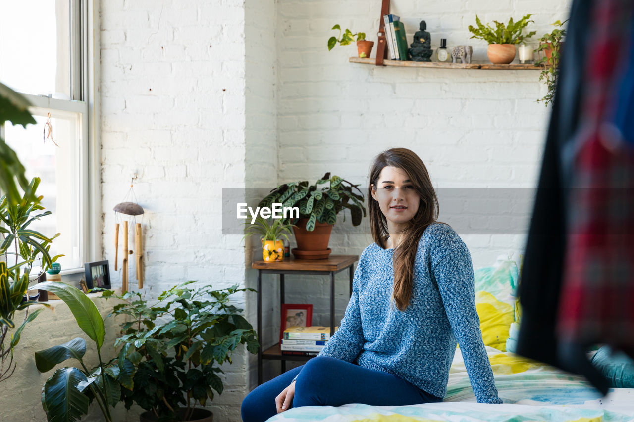 Portrait of smiling woman sitting on bed at home