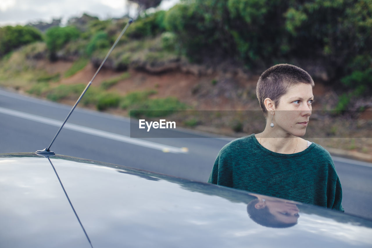 Woman looking away while standing by car on roadside