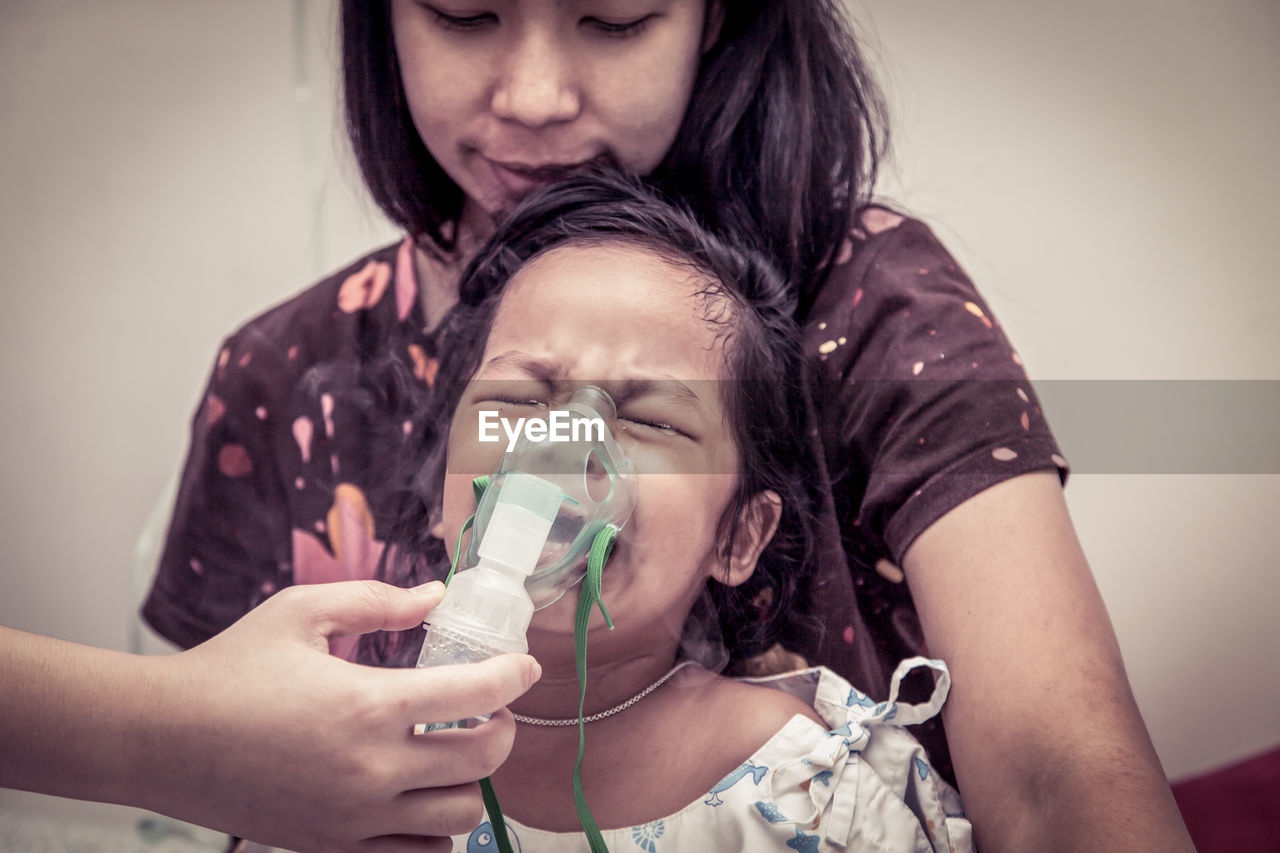 Cropped image of doctor putting mask on crying girl