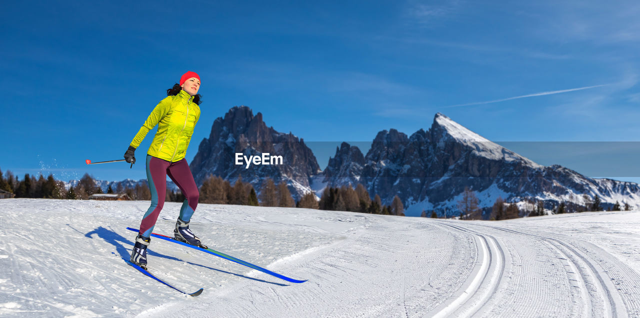 WOMAN SKIING ON SNOWCAPPED MOUNTAINS AGAINST SKY
