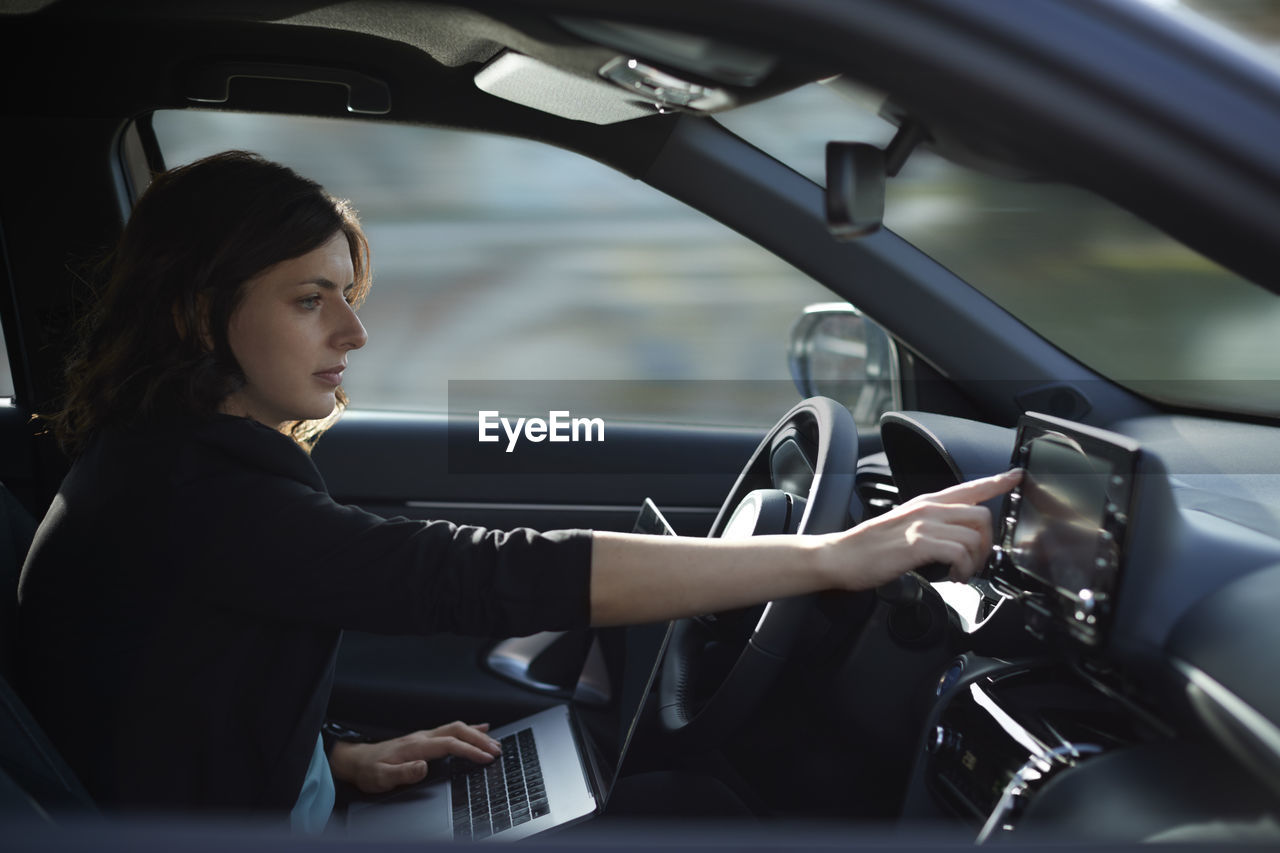 Businesswoman with laptop using navigation device in driverless car