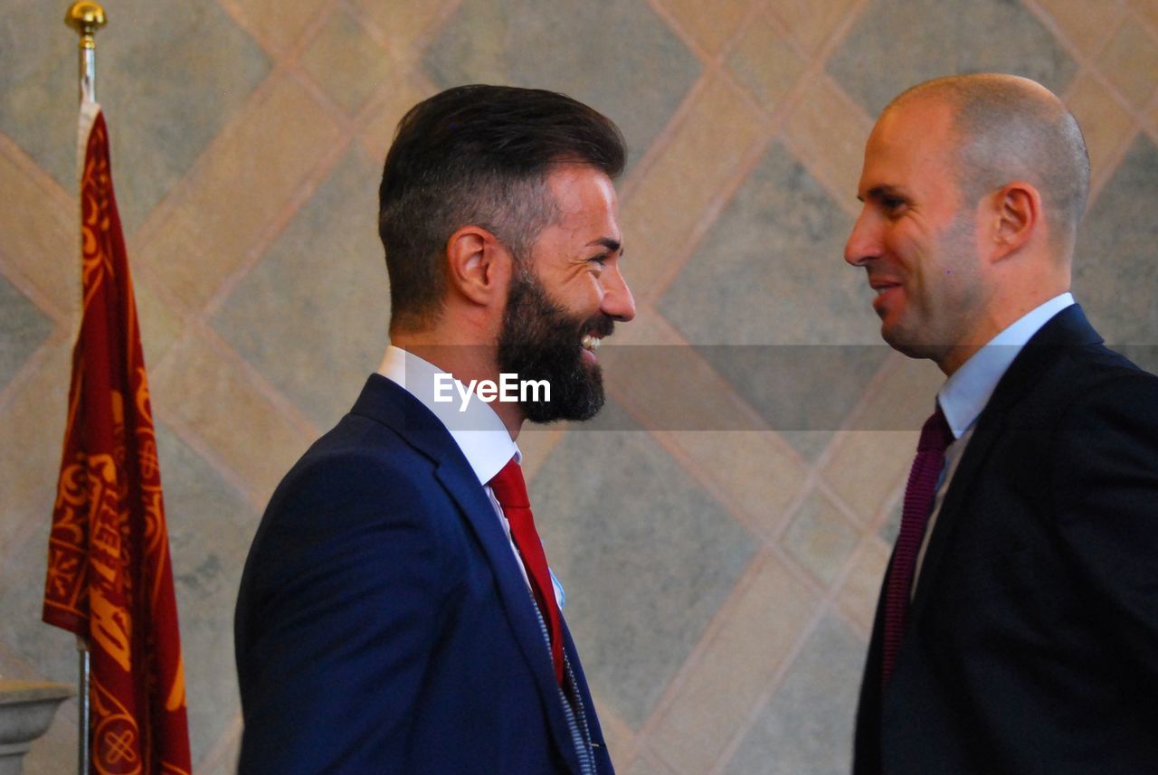 Side view of smiling businessmen against wall