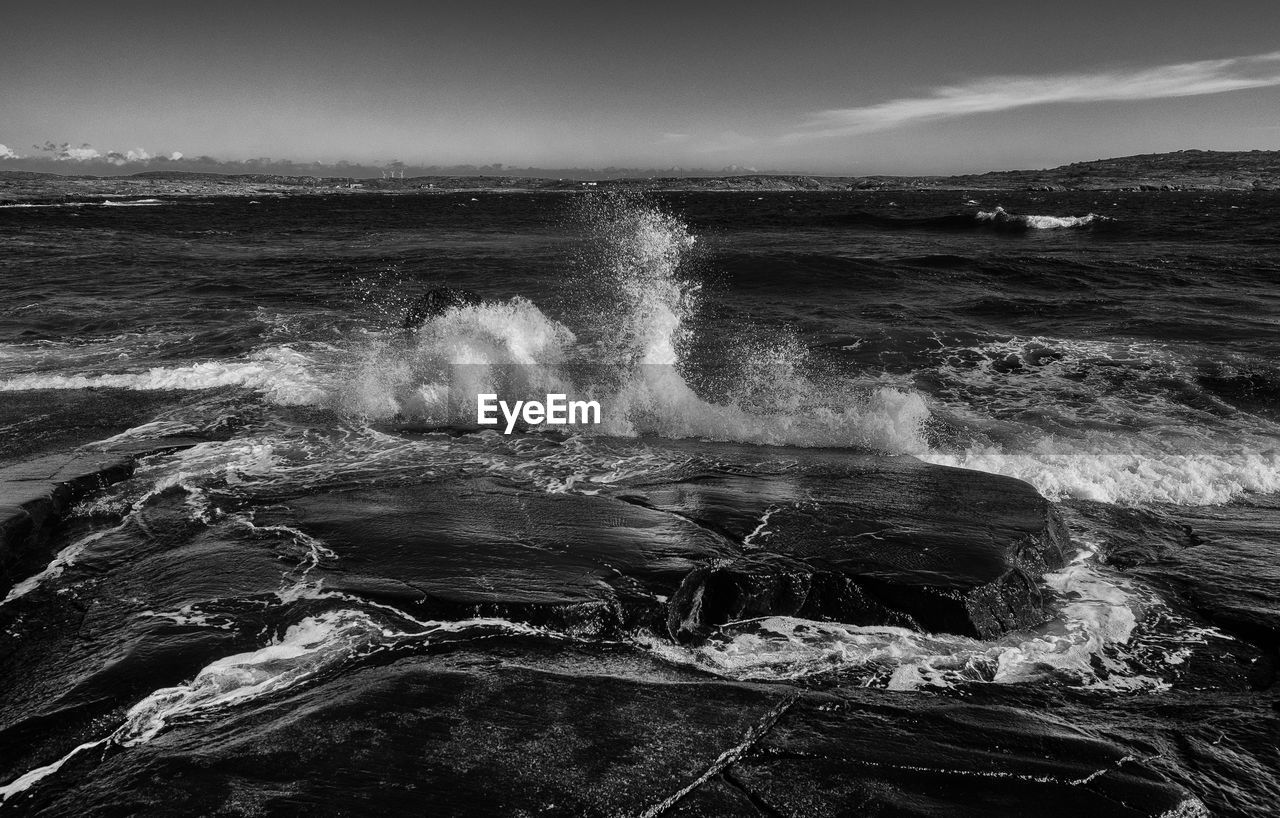 Waves splashing on rocks against sky