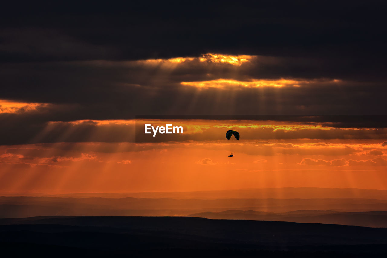 Silhouette of person paragliding over sea against sky during sunset