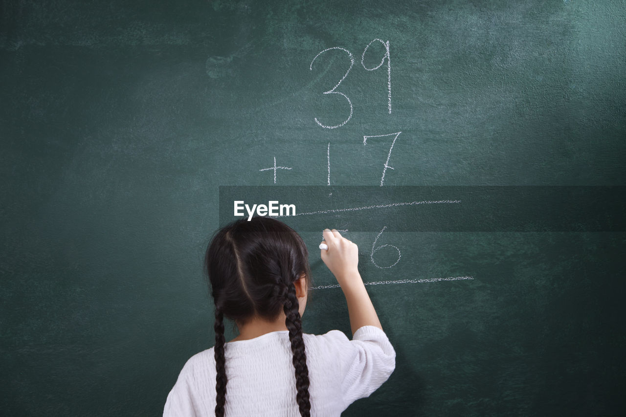 Rear view of girl learning mathematics on blackboard