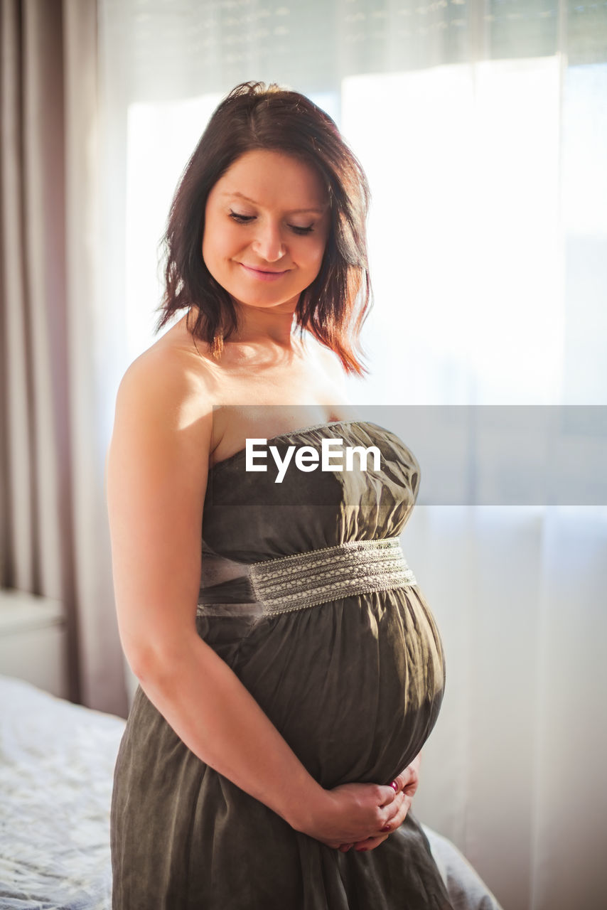 Pregnant woman in dress against window in bright room