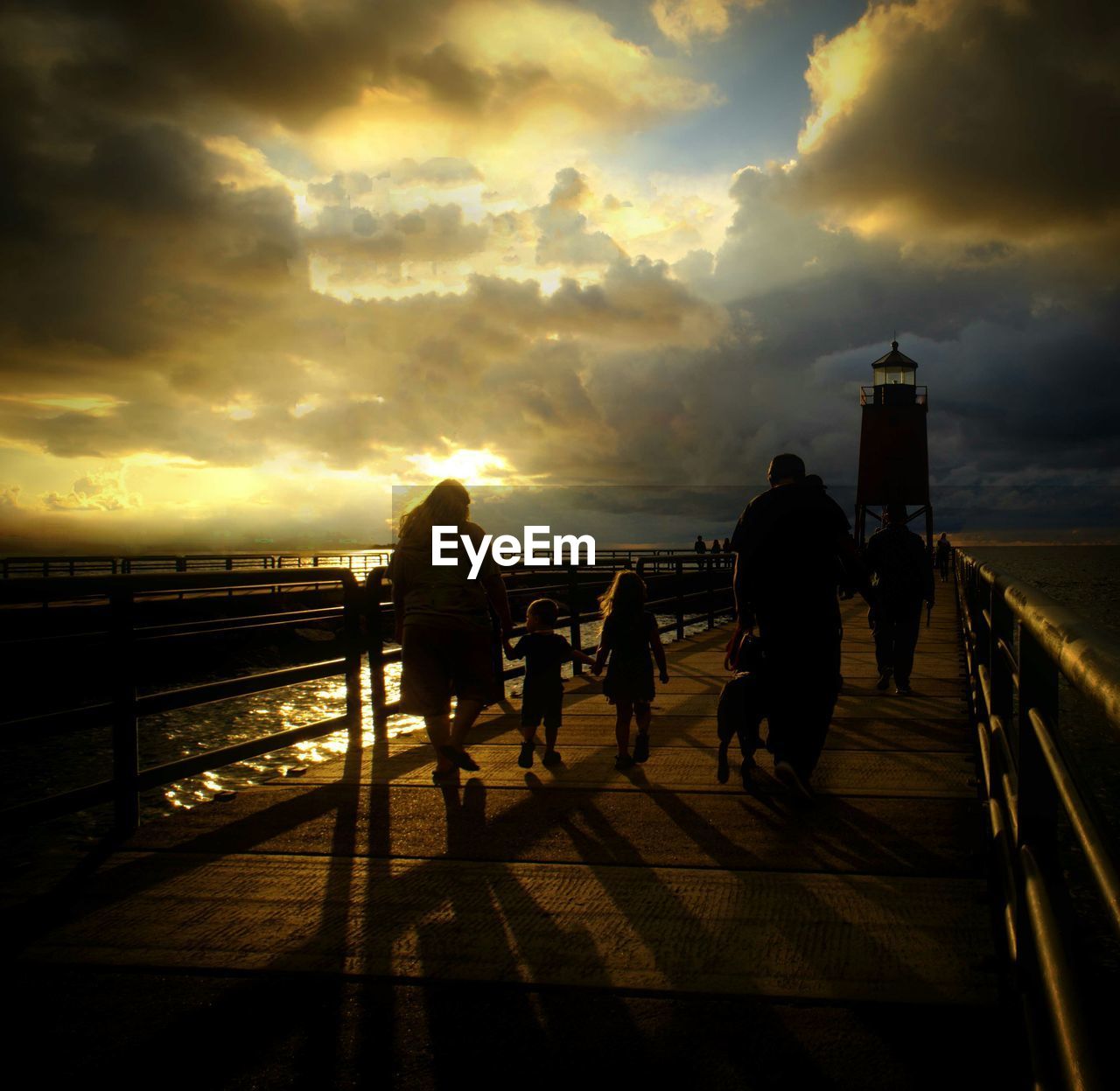 PEOPLE WALKING ON ROAD AGAINST CLOUDY SKY AT SUNSET