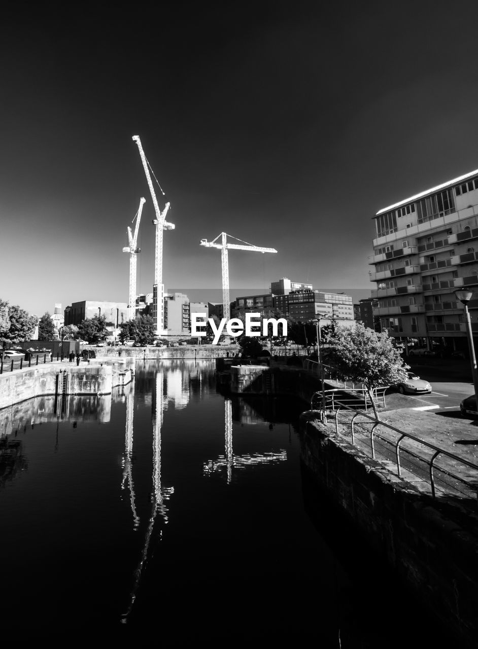 Cranes reflecting in canal against sky