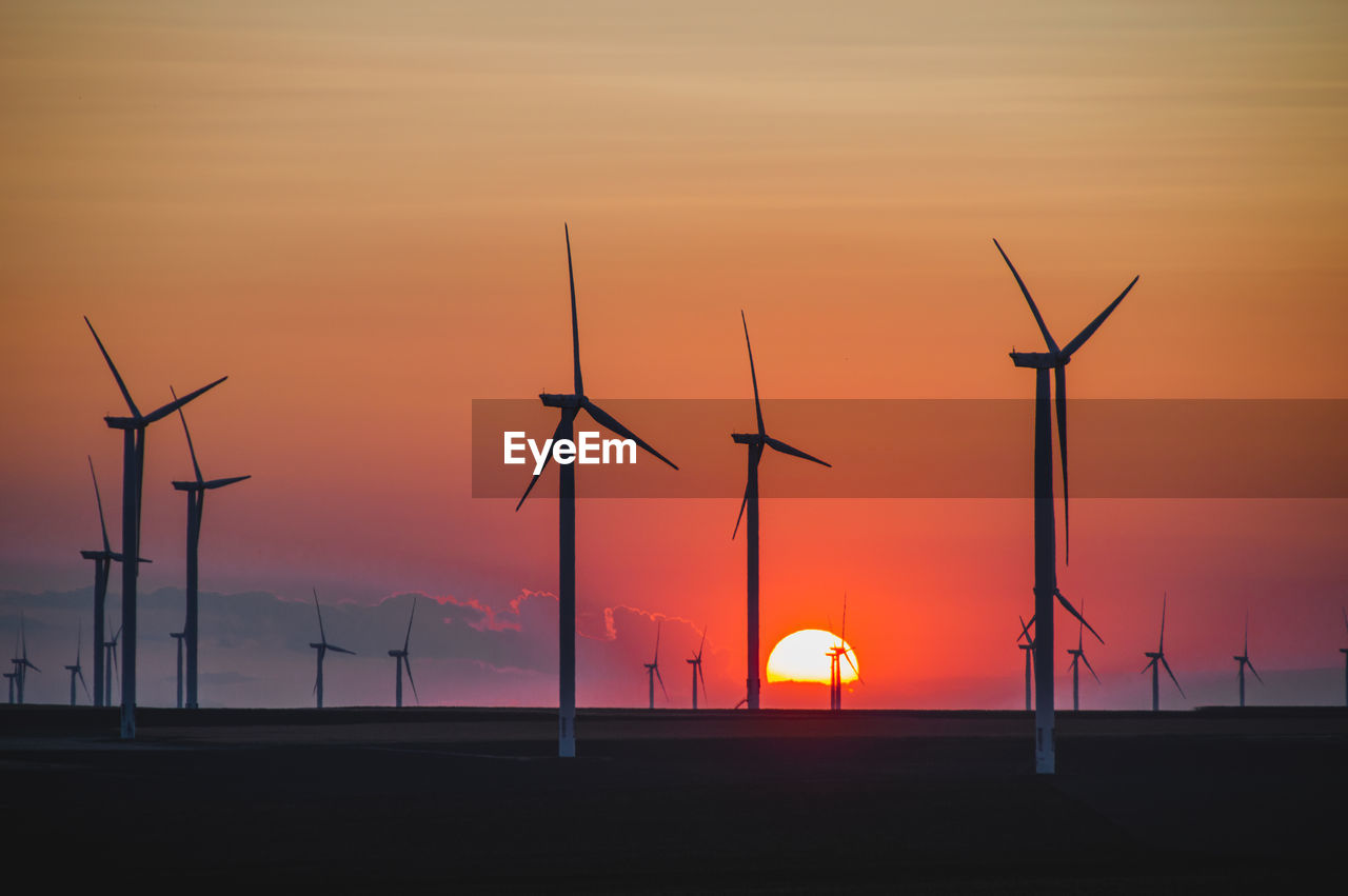 Silhouette wind turbines on field against orange sky