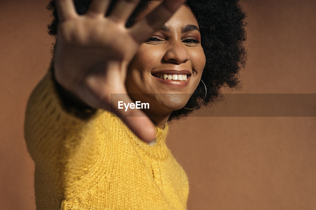 Portrait of young woman standing against brown background