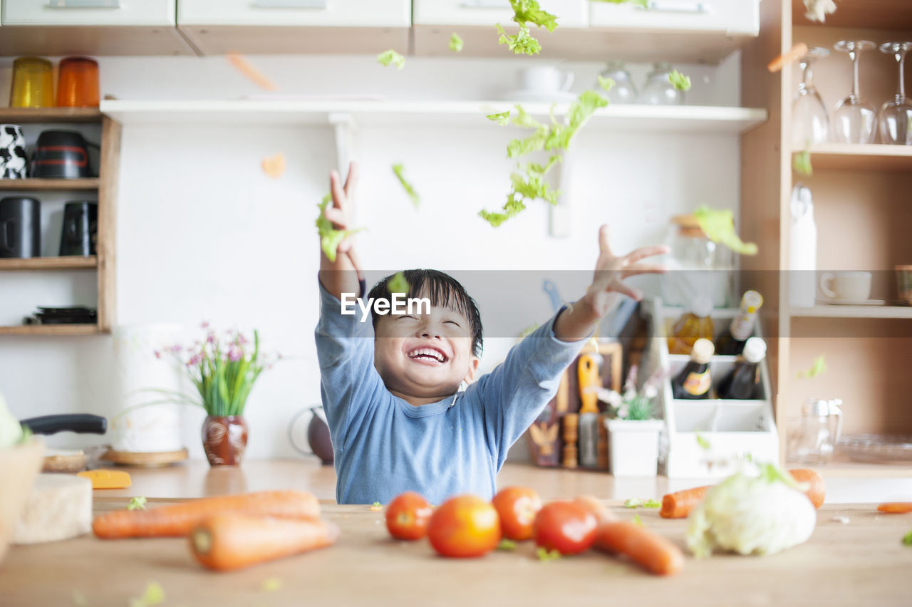 Happy boy tossing vegetables in kitchen at home