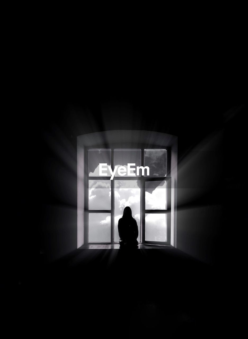 Silhouette woman sitting at window in darkroom