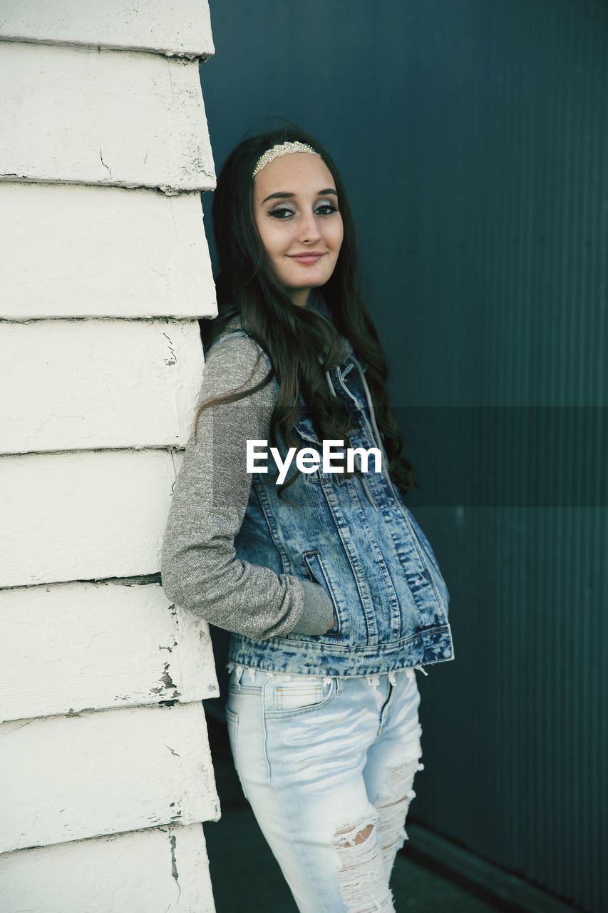 Portrait of young woman standing against wall