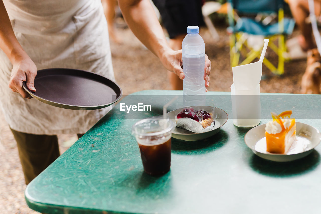 Waiter serving a bottle of water on table in cafe outdoor.