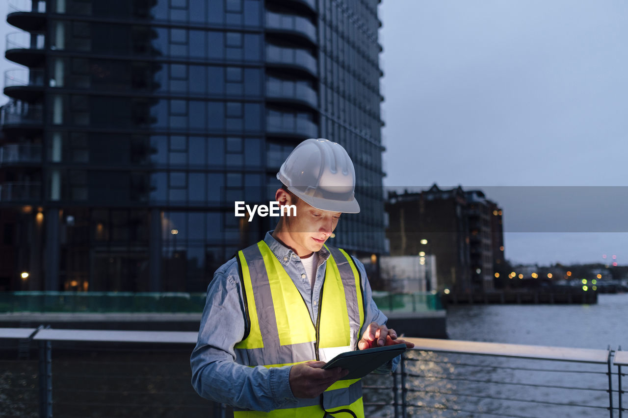 Engineer wearing hardhat using tablet pc by railing